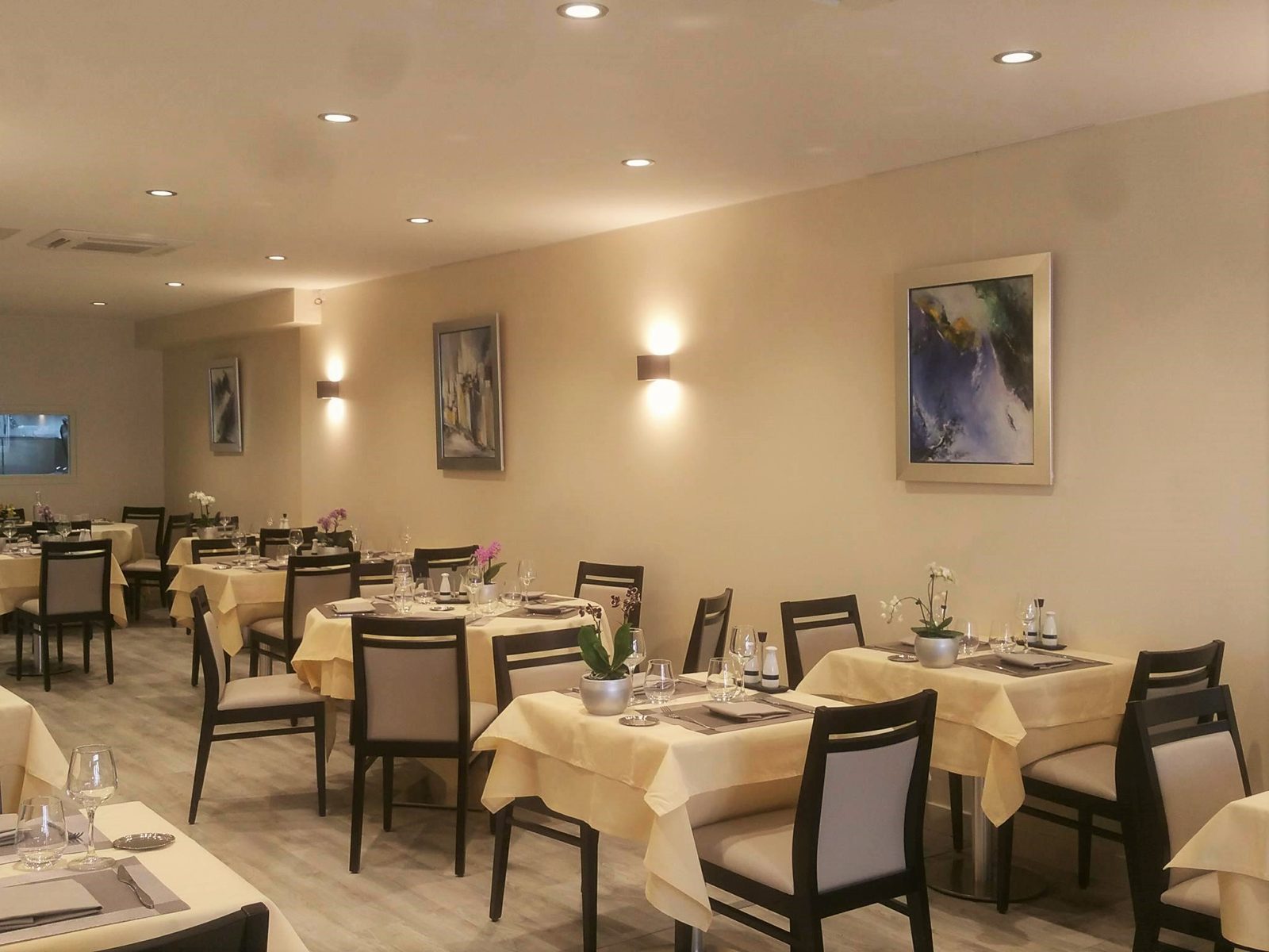 La salle vue de côté : tables dressées, tableaux aux tons bleus et appliques, couverts alignés